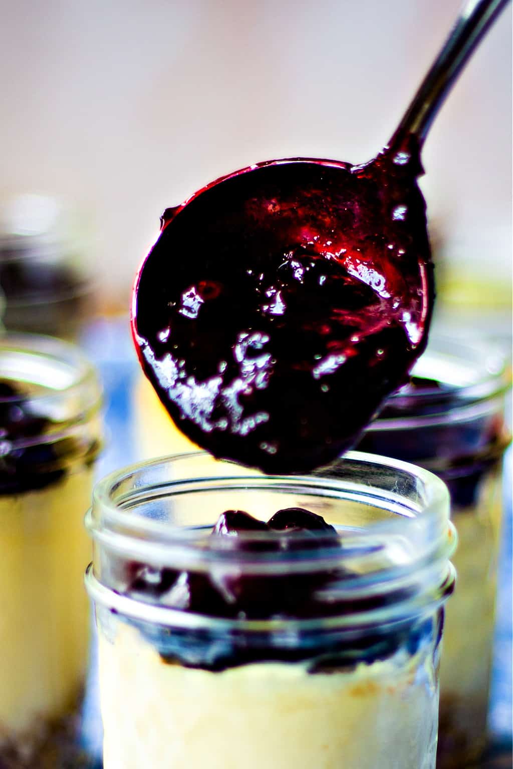 spooning blueberry topping on top of cheesecake in a jar