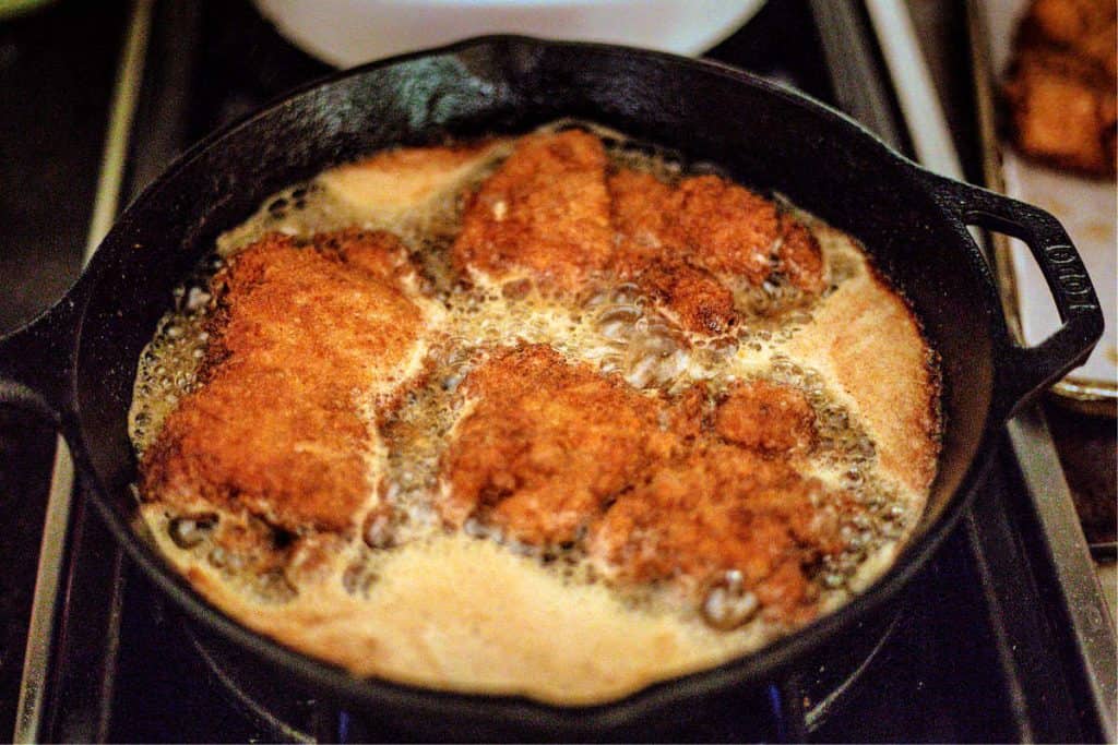 chicken thighs frying in a cast iron skillet