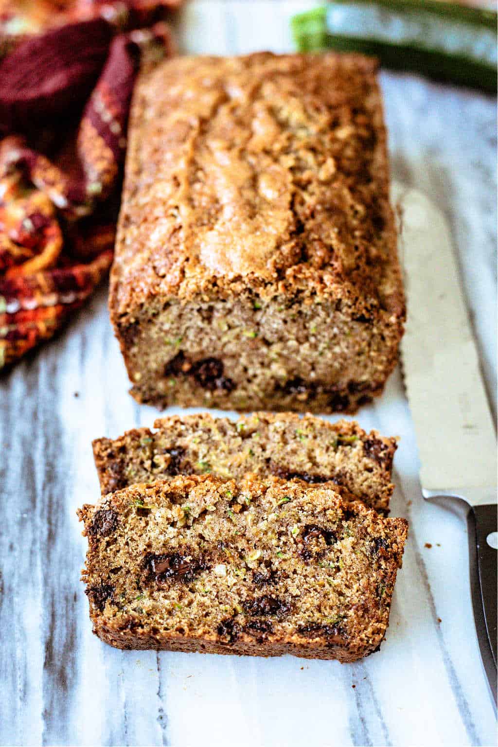 chocolate chip Zucchini Bread on a marble board with two cut slices and serrated knife