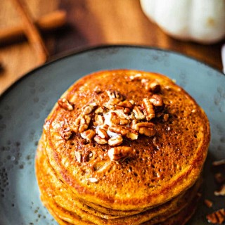 Pumpkin Spice Pancakes with maple syrup and toasted pecans on a blue plate