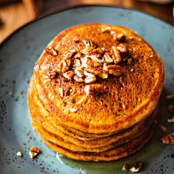 Pumpkin Spice Pancakes with maple syrup and toasted pecans on a blue plate
