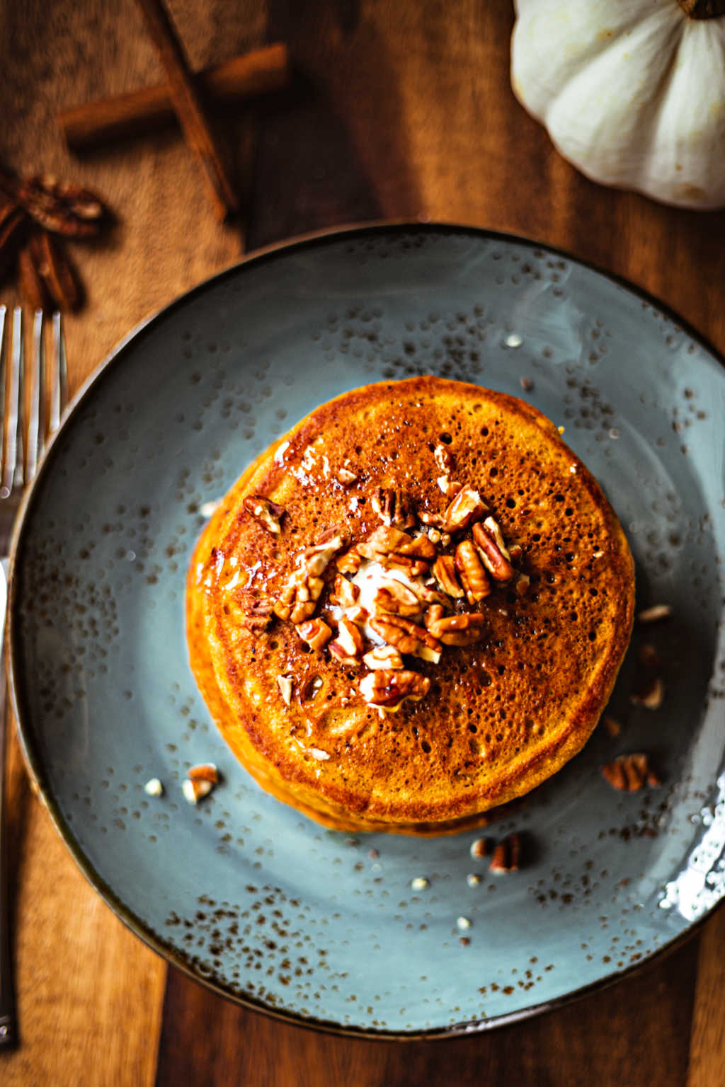 Pumpkin Spice Pancakes with maple syrup and toasted pecans on a blue plate