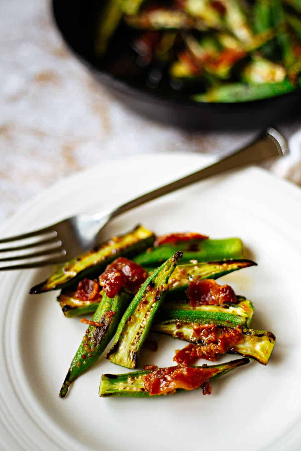 roasted okra with warm bacon vinaigrette on a white plate with a fork