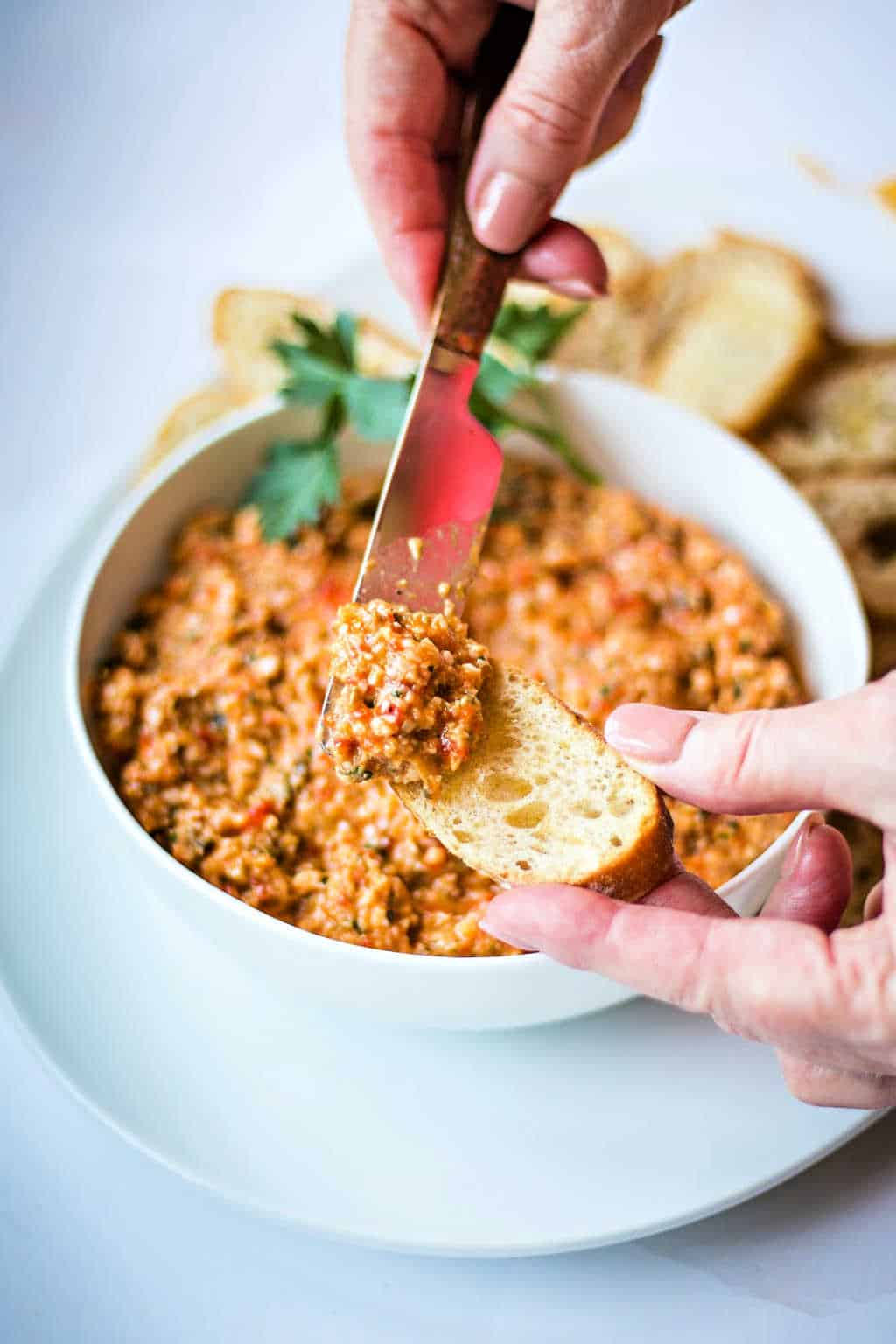 spreading roasted red pepper tapenade on a baguette