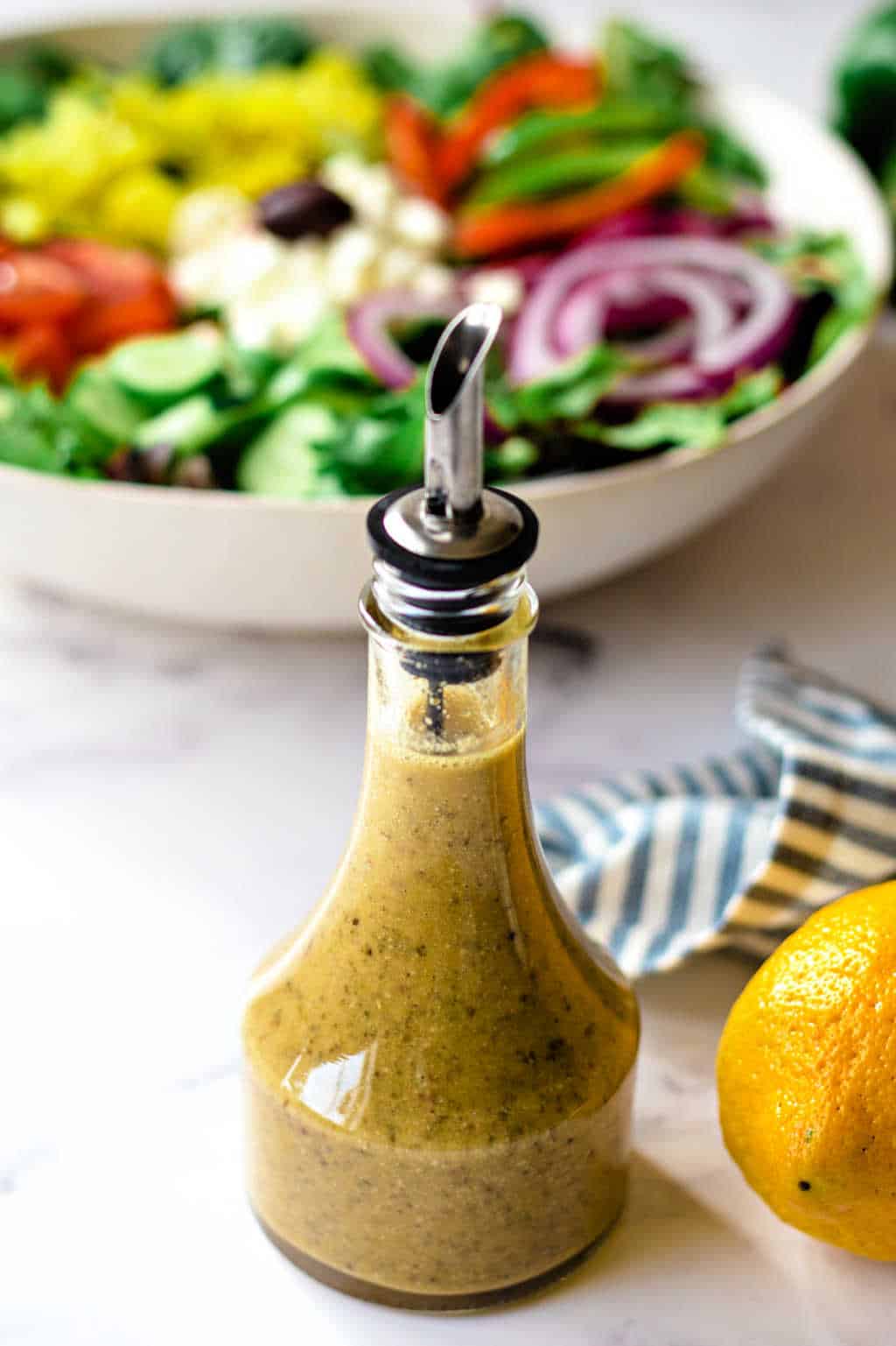 greek salad dressing with a bowl of salad in the background