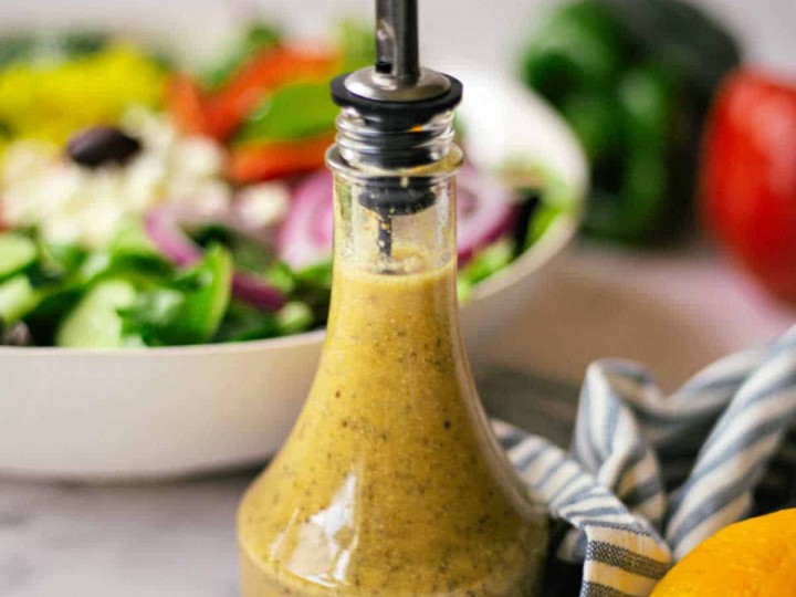 greek salad dressing with a bowl of salad in the background