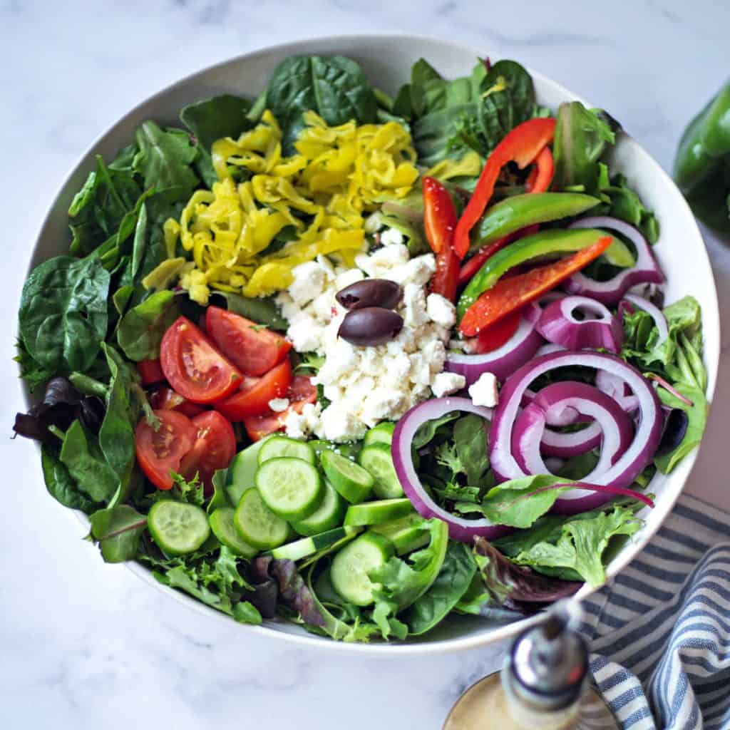 A bowl of salad on a plate, with Greek salad ingredients
