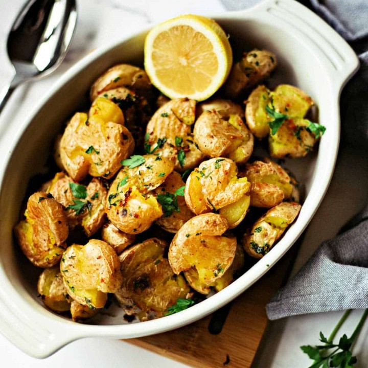 Lemon Garlic Smashed Potatoes with a lemon slice in a white dish