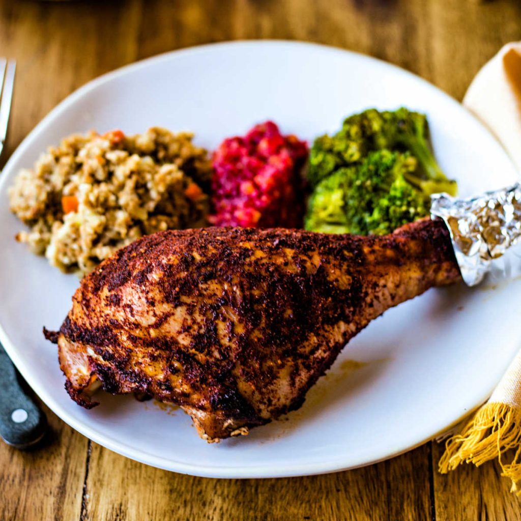 a roasted turkey leg on a white plate with sides on a wooden table