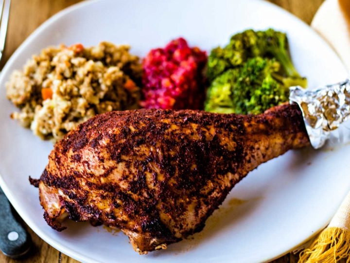 a roasted turkey leg on a white plate with sides on a wooden table