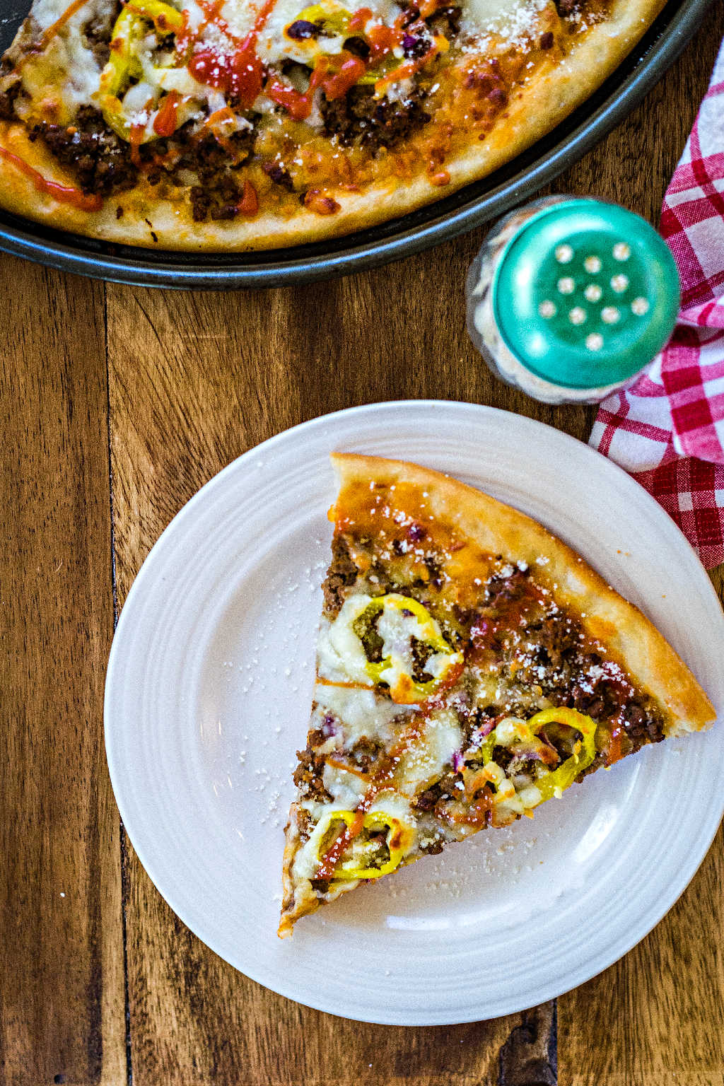 a slice of cheeseburger pizza on a white plate on a wooden table