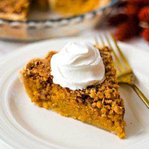 a slice of sweet potato pie with a dollop of whipped cream on a white plate