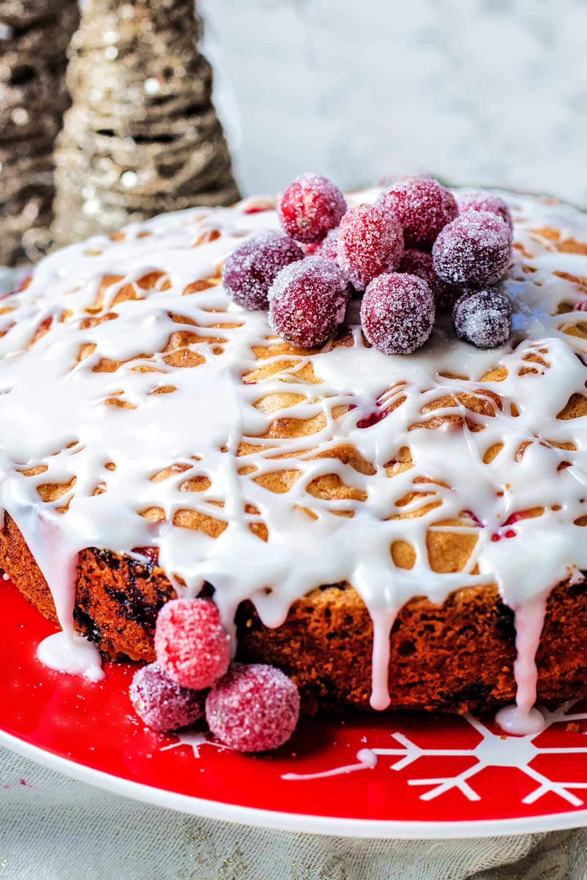 A cranberry cake with vanilla glaze and candied cranberries on top sitting on a cake stand on a table.