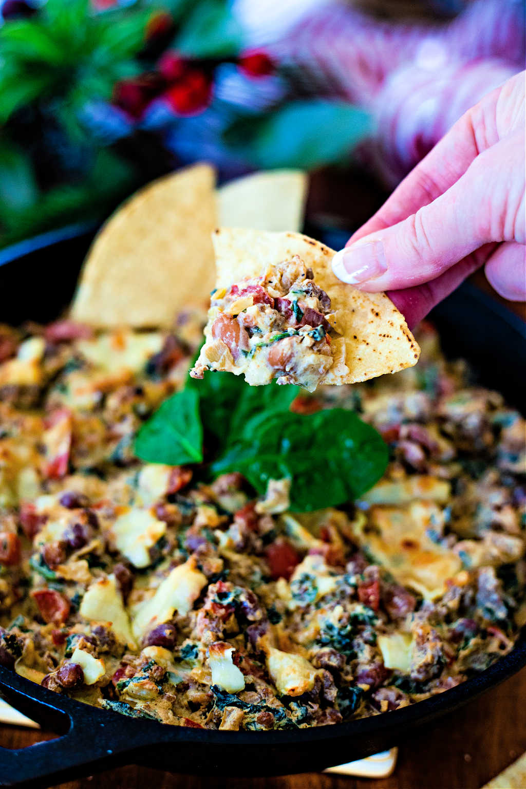 dipping a tortilla chip into Sausage, Bean, and Spinach Dip in a cast iron skillet