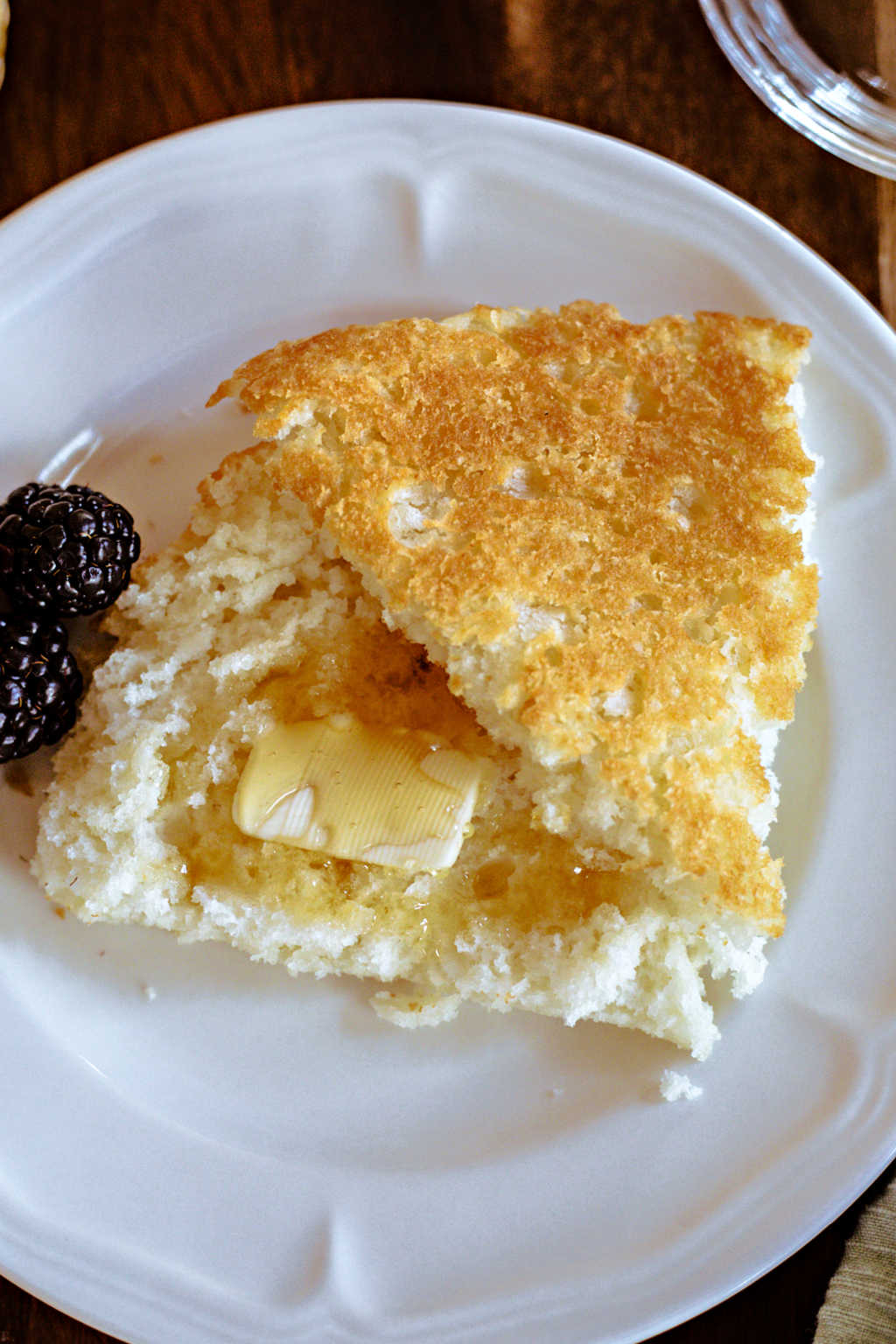 a slice of biscuit bread split open with butter and honey on a white plate