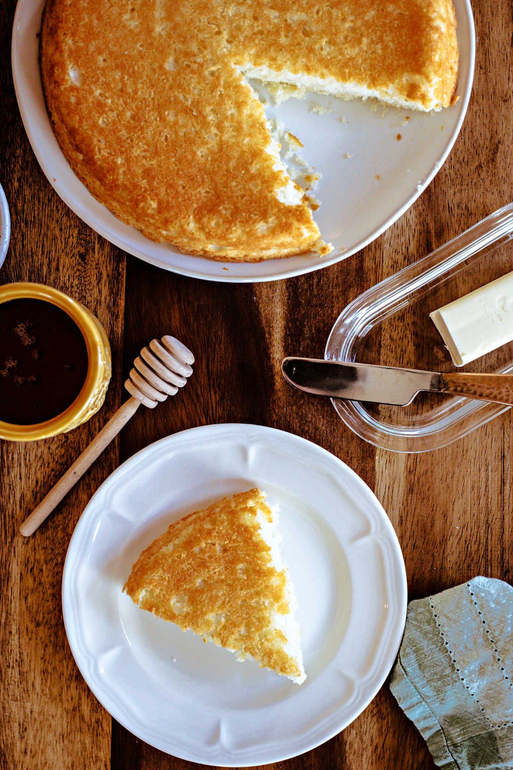 a wooden table with a plate of biscuit bread, butter, and honey