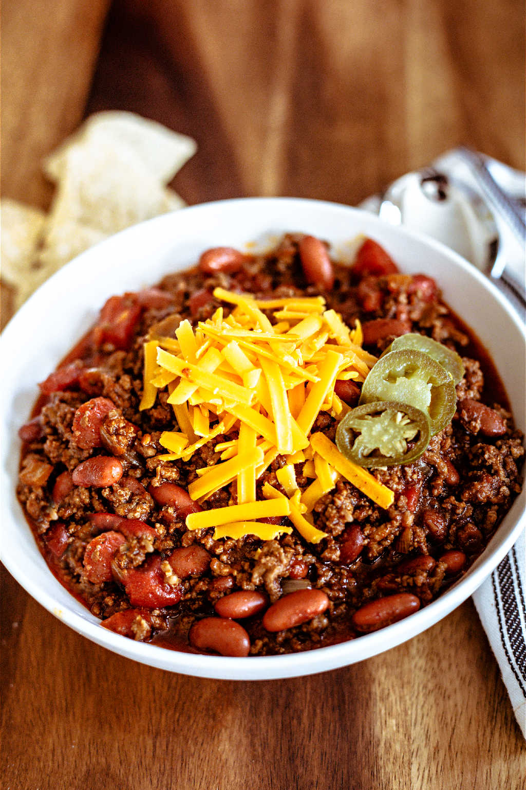 ground beef chili in a white bowl topped with cheese and jalapeno slices