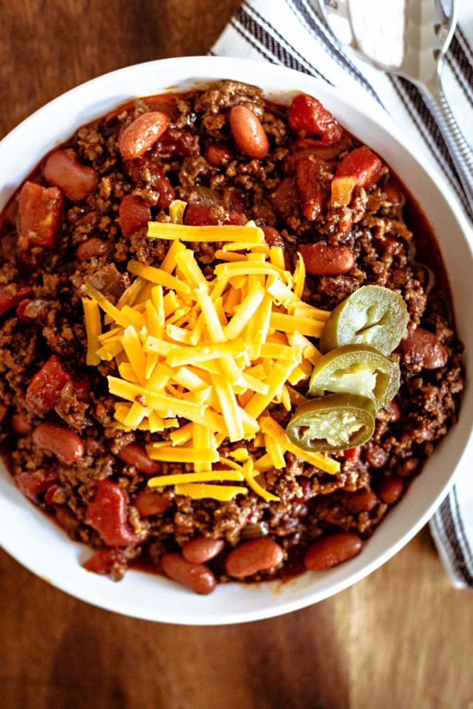 ground beef chili in a white bowl topped with cheese and jalapeno slices