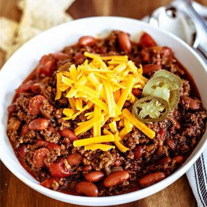 ground beef chili in a white bowl topped with cheese and jalapeno slices