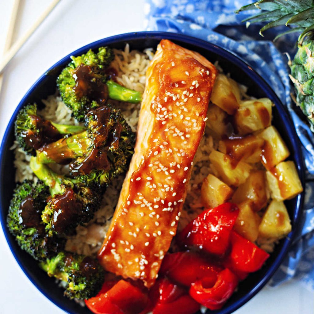 teriyaki salmon in a bowl with brown rice, roasted broccoli, red bell pepper, and pineapple