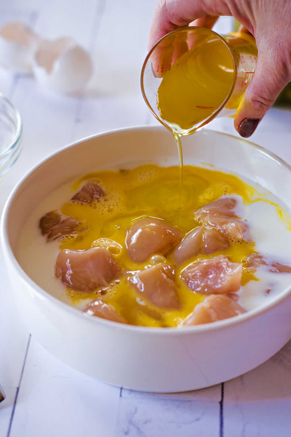 pouring dill pickle juice into a bowl of cut up chicken to marinate.