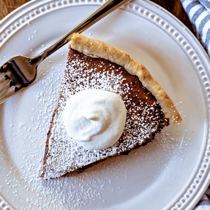 a slice of chocolate chess pie on a white plate on a wooden table.