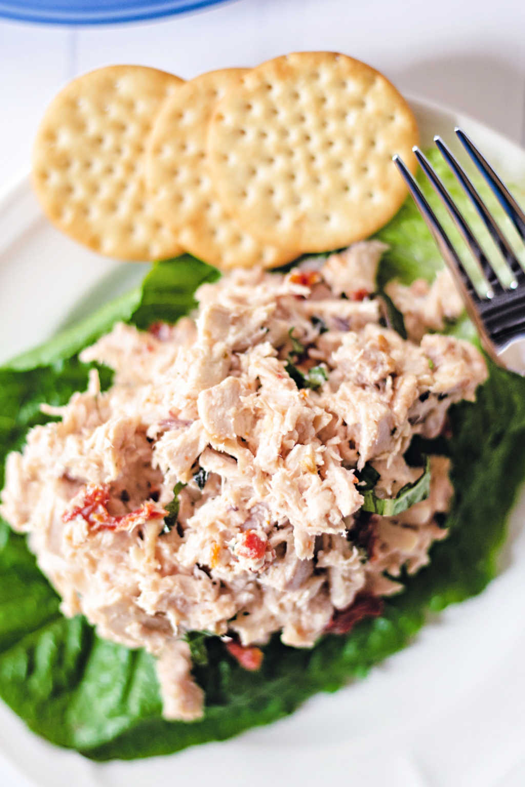 rotisserie chicken salad on a lettuce leaf on a white plate with crackers