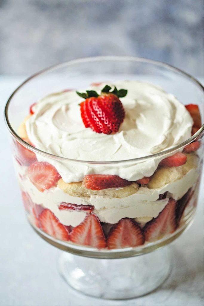 strawberry trifle with whipped cream and strawberry garnish on top in a glass trifle bowl.
