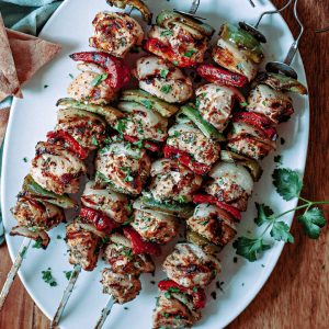 four skewers of greek chicken kebabs on a white platter on a wooden table.