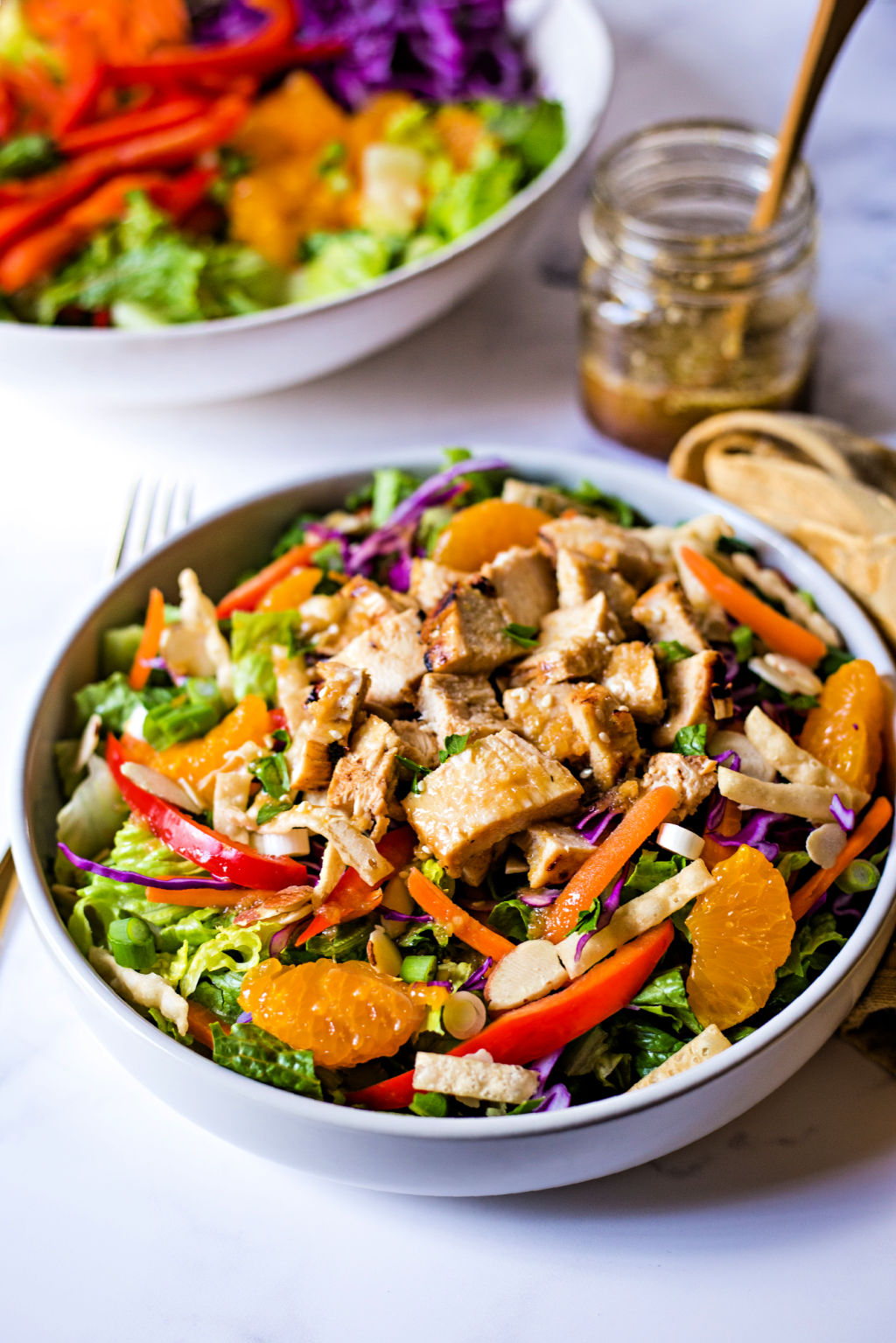 Asian Sesame Salad with Chicken in a bowl with a fork and jar of dressing on a table.