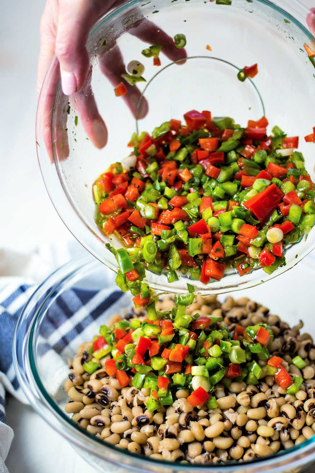 pouring vinaigrette into a bowl of cooked black eyed peas.