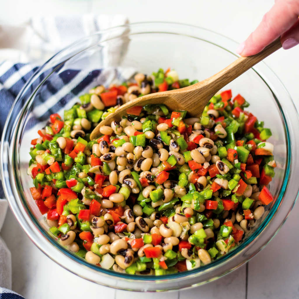 stirring vinaigrette into black eyed peas with a wooden spoon for salad.