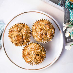 three chocolatey coconut banana muffins on a white plate on a table.