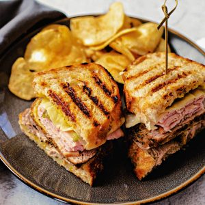 Sandwich Cubano on a gray plate with potato chips on the table.