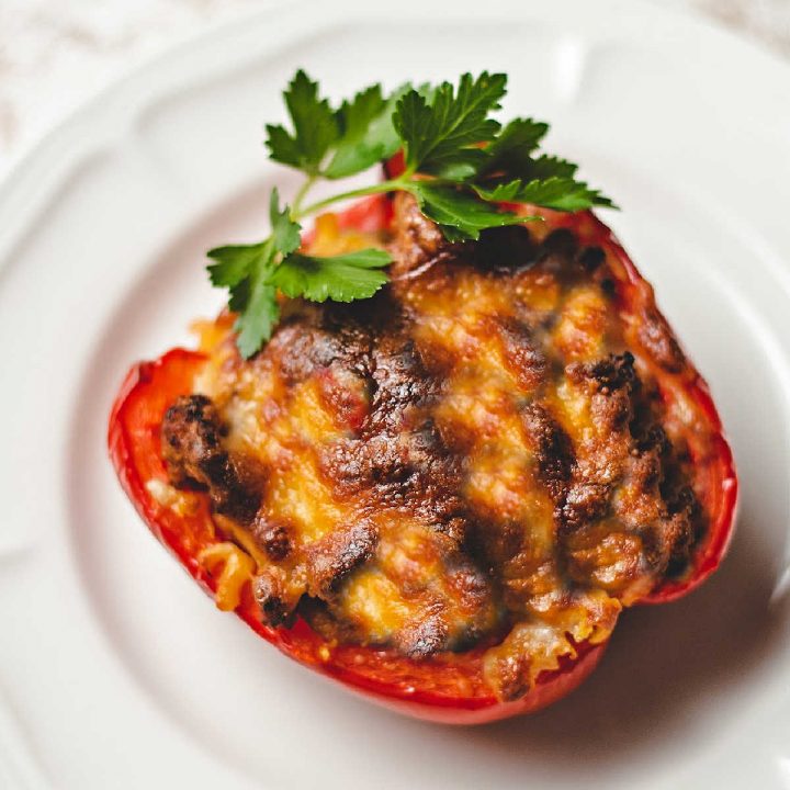 a keto stuffed red bell pepper on a white plate garnished with parsley on a kitchen counter.