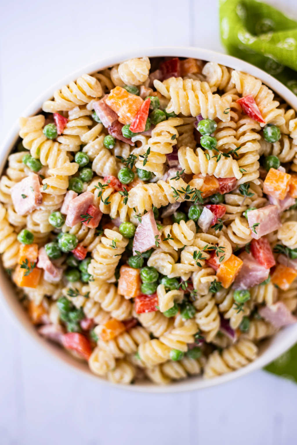 macaroni salad with peas in a white bowl on a white countertop with a green napkin.