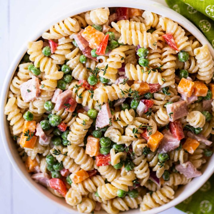 macaroni salad with peas in a white bowl on a white countertop with a green napkin.