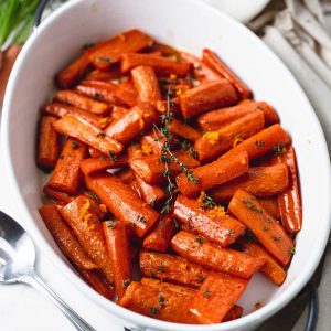 roasted carrots with honey in a white dish with a spoon on a table with a linen napkin.