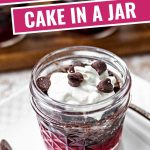 chocolate cherry dump cake in a jar with whipped cream and chocolate chips on a table.