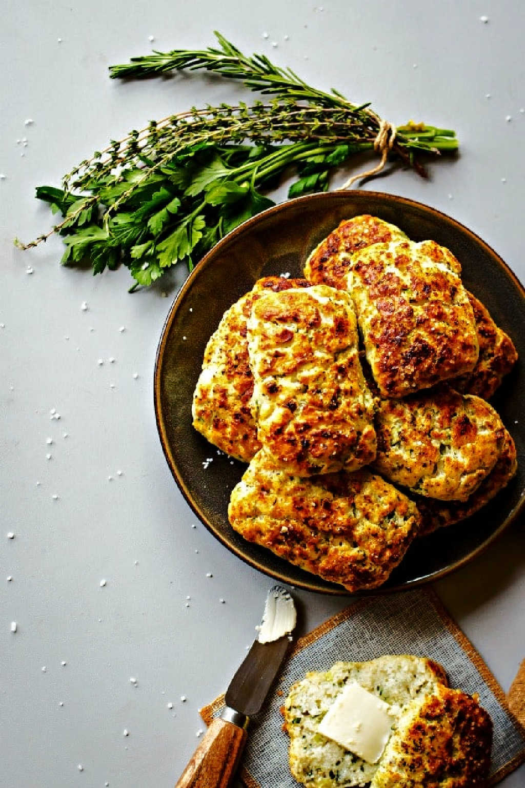 ricotta herb savory scones on a plate on a table with a bundle of fresh herbs.