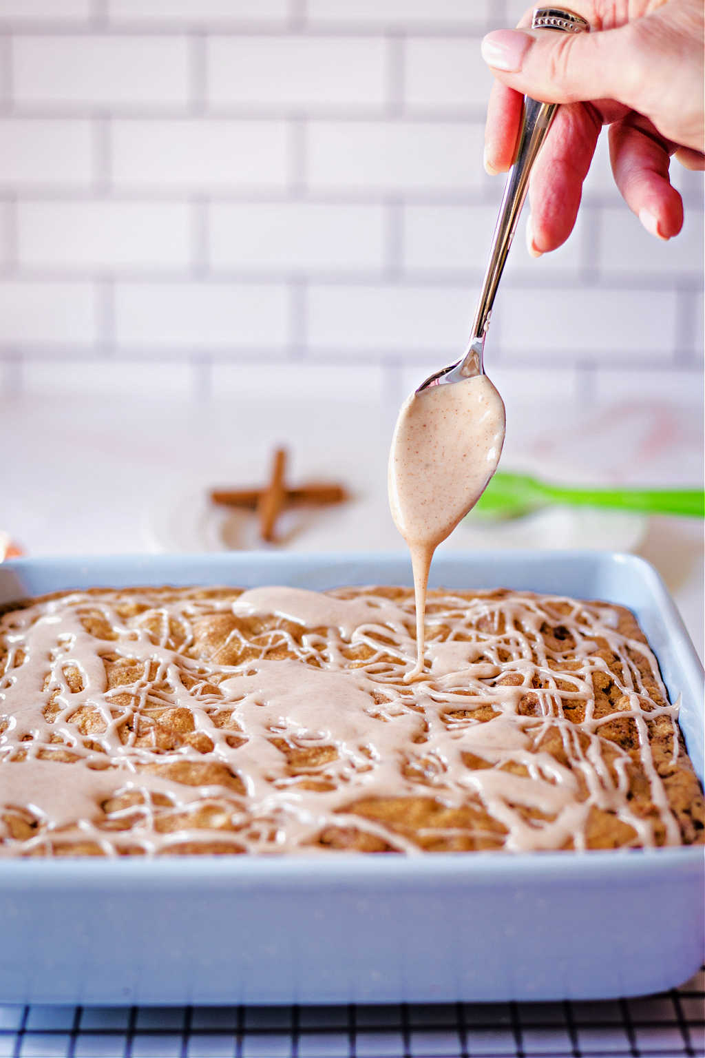 a spoon drizzling cinnamon glaze on a warm apple walnut snack cake.