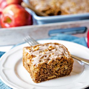 a slice of apple walnut cake on a white plate on a table.