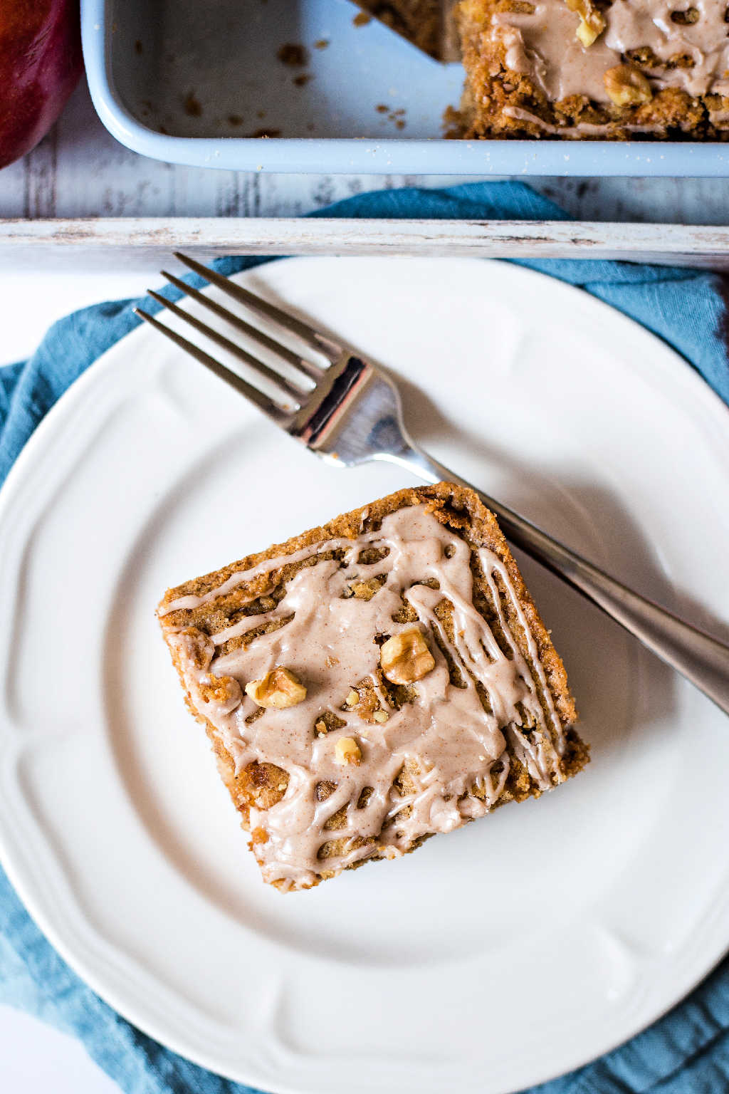 a slice of apple walnut cake on a white plate on a table with a tray.