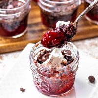 a spoon of chocolate cherry dump cake in a jar on a table.
