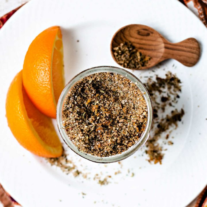 citrusy salmon rub in a glass jar on a white plate with orange wedges and a wooden spoon.
