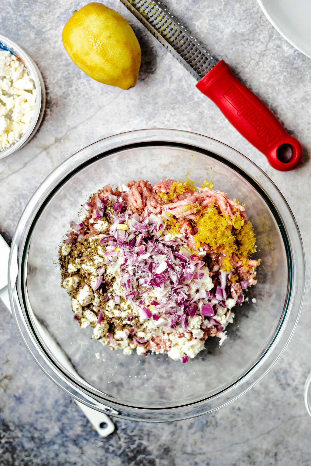 mixing ingredients into ground turkey in a glass bowl for Greek Turkey Burgers.