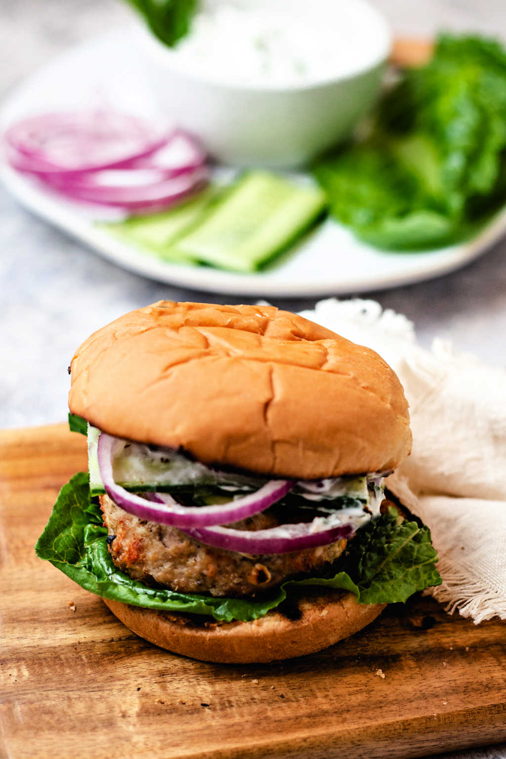 a greek turkey burger on a wooden board on a table.