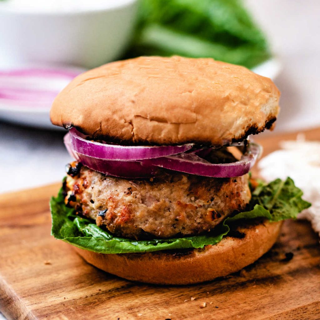 a greek turkey burger with red onion on a wooden board on a table.