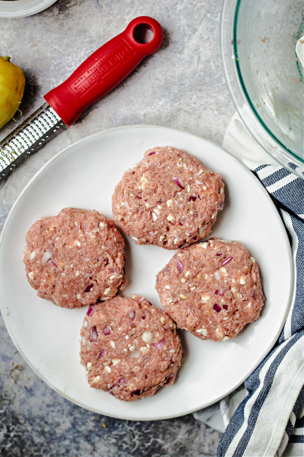 uncooked Greek turkey burgers on a white plate on a table.