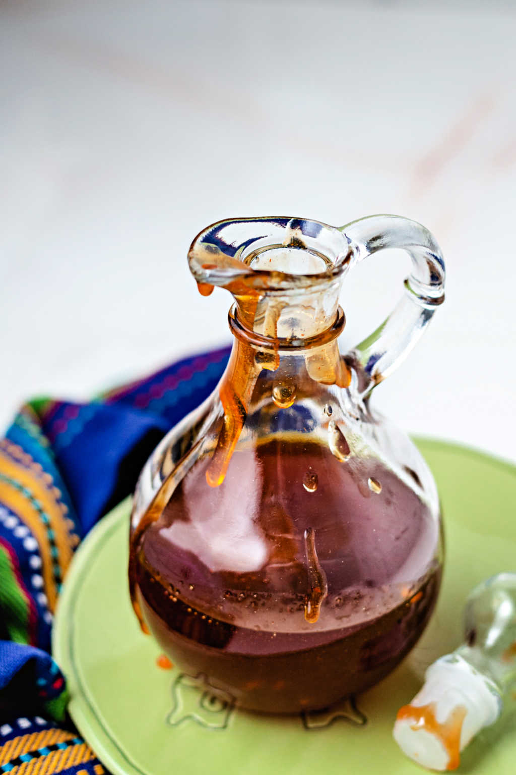 honey sriracha sauce in a glass decanter sitting on a green plate.